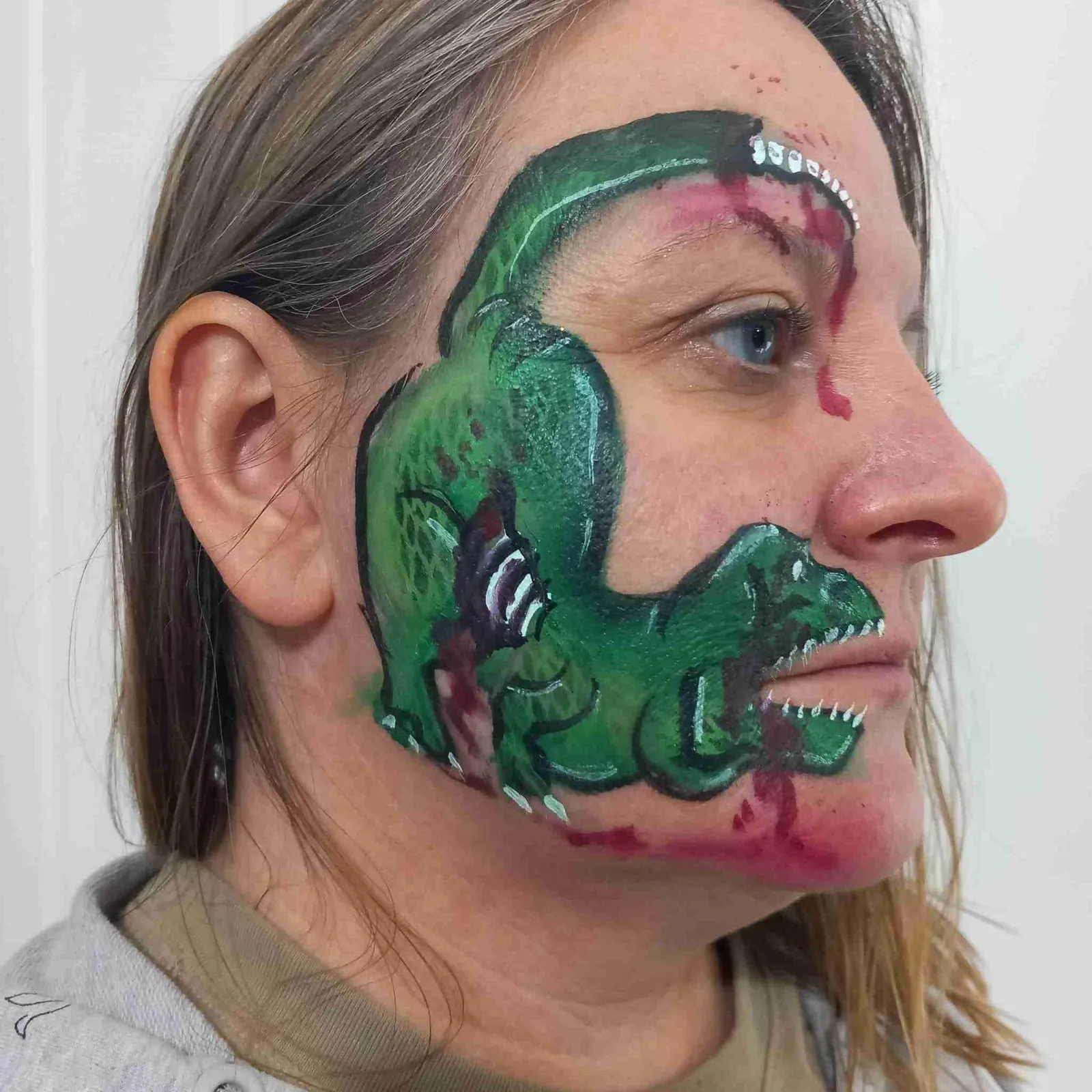 A green dinosaur painted across a face