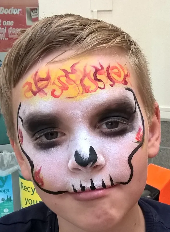 A boy painted as a skull wreathed in flames