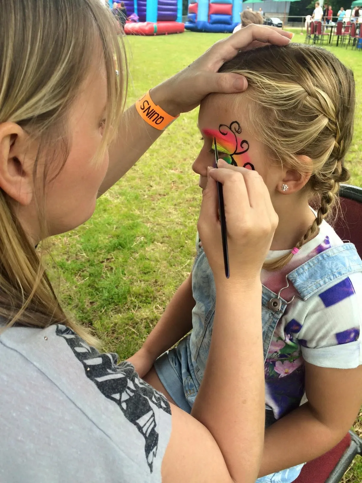 Christine painting a bright design on a child's face at an outdoor event